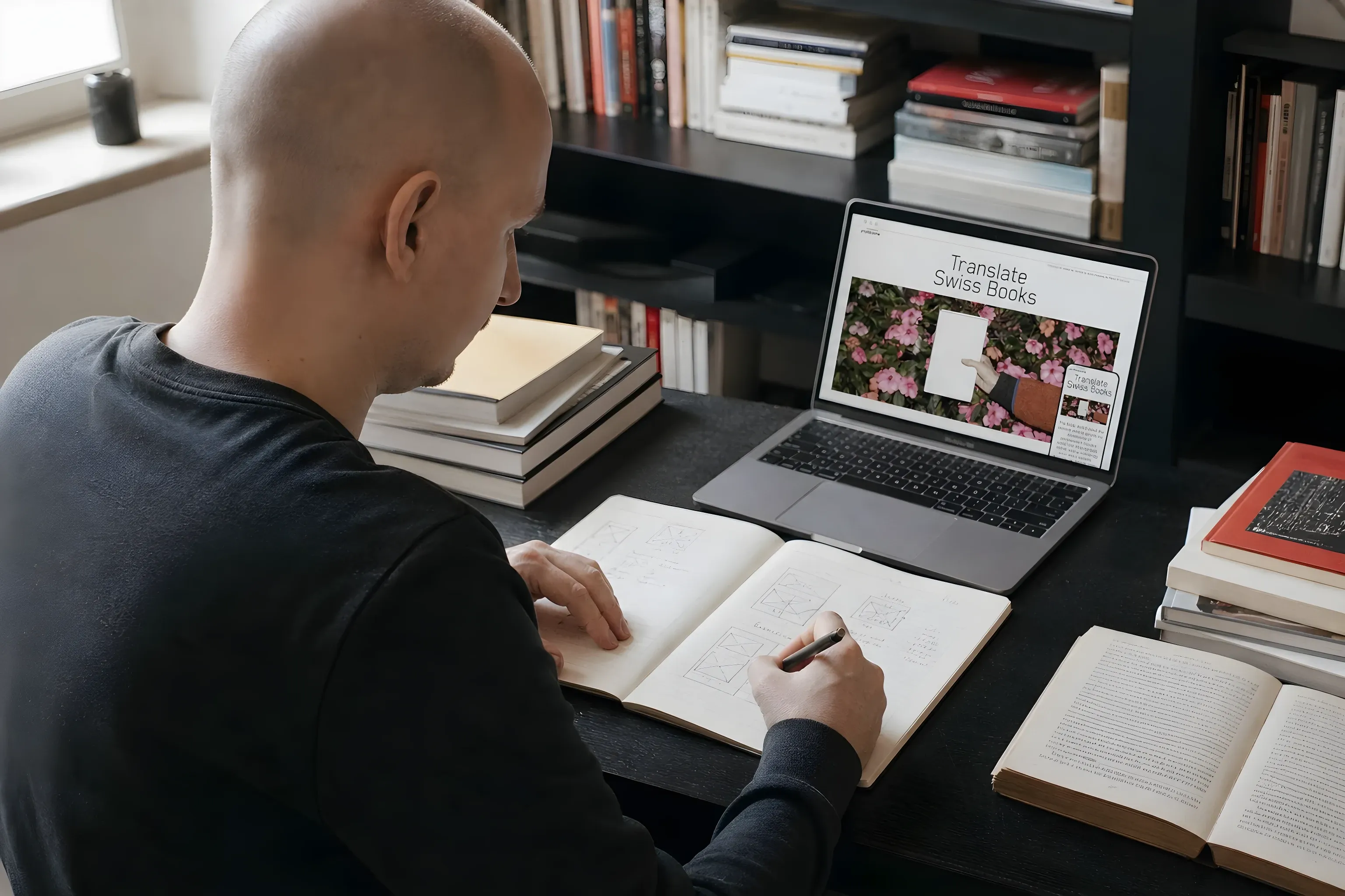 Me sketching layouts in a notebook beside the Translate Swiss Books site